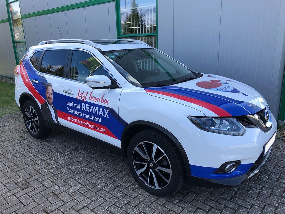 Vor einem Gebäude ist ein Remax-Auto geparkt.