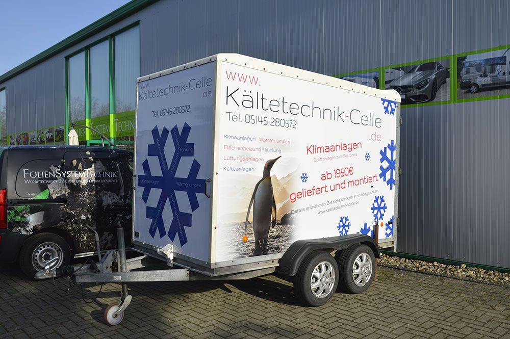 Vor einem Gebäude steht ein Anhänger mit einem Pinguin und einer Schneeflocke darauf.