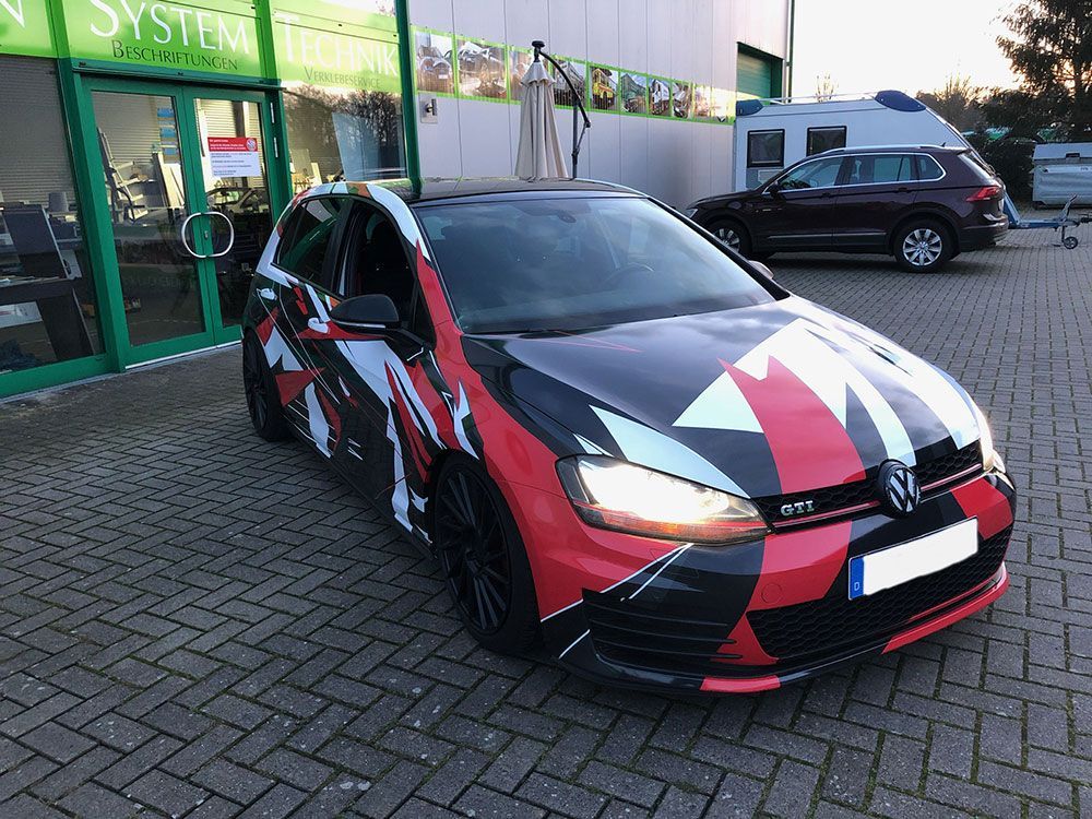 Vor einem Gebäude parkt ein rot-schwarzes Auto.