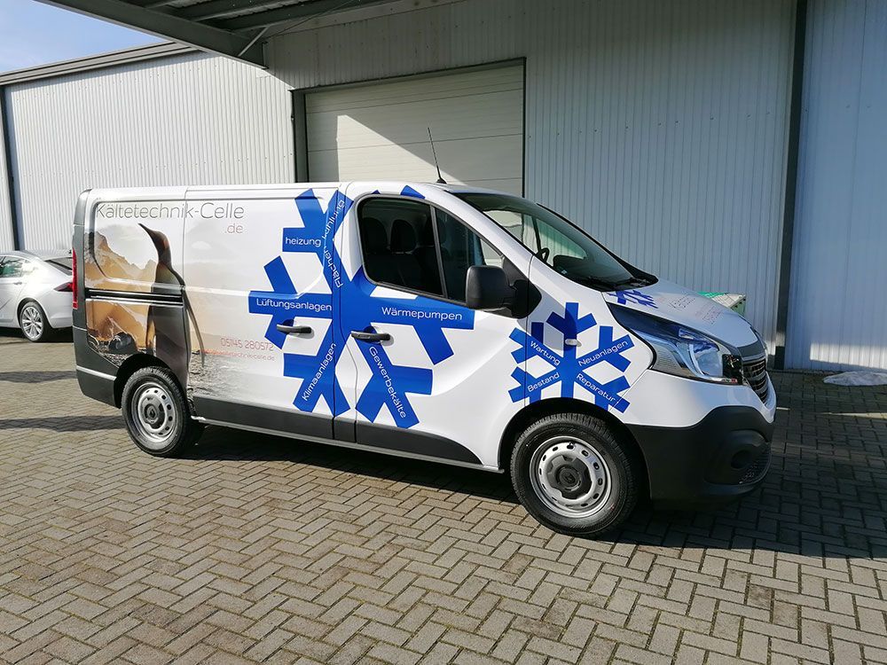 Ein weißer Lieferwagen mit blauen Schneeflocken an der Seite steht vor einem Gebäude.