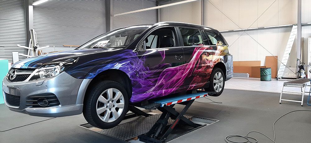 Ein lila-blaues Auto steht auf einer Hebebühne in einer Garage.