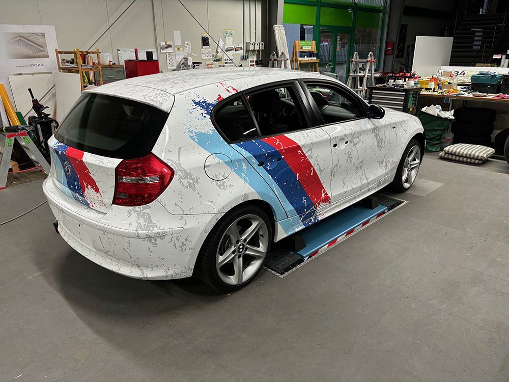 Ein weißes Auto mit roten, blauen und weißen Streifen an der Seite steht in einer Garage.