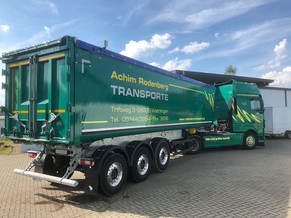 Ein grüner Muldenkipper steht vor einem Gebäude.