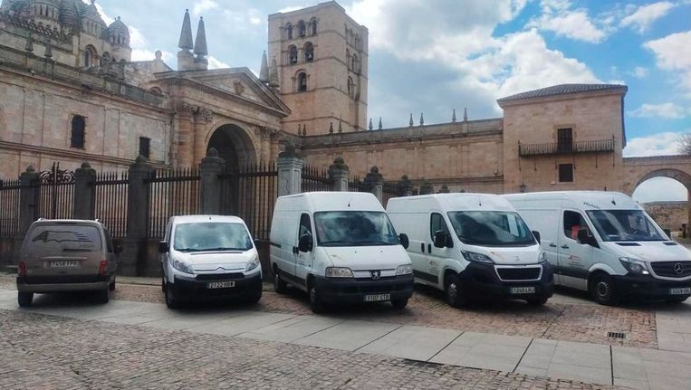 Una fila de furgonetas blancas están estacionadas frente a un edificio.