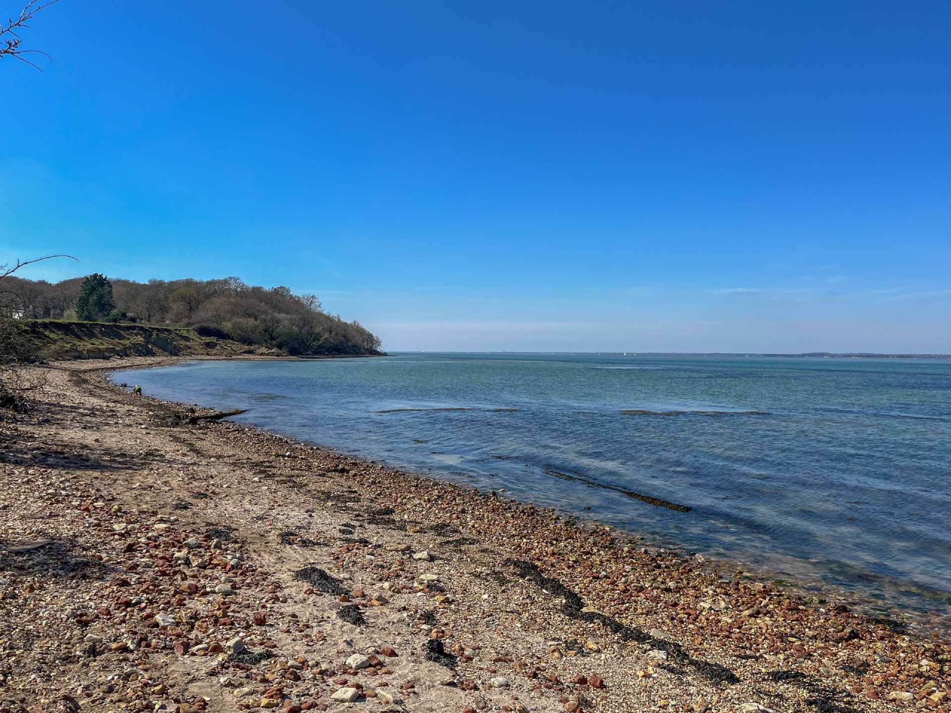 Rocky shoreline meets calm ocean under a pale blue sky.