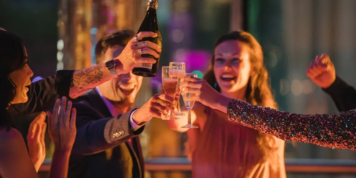 People toasting with champagne glasses at a party, one person is opening a bottle.