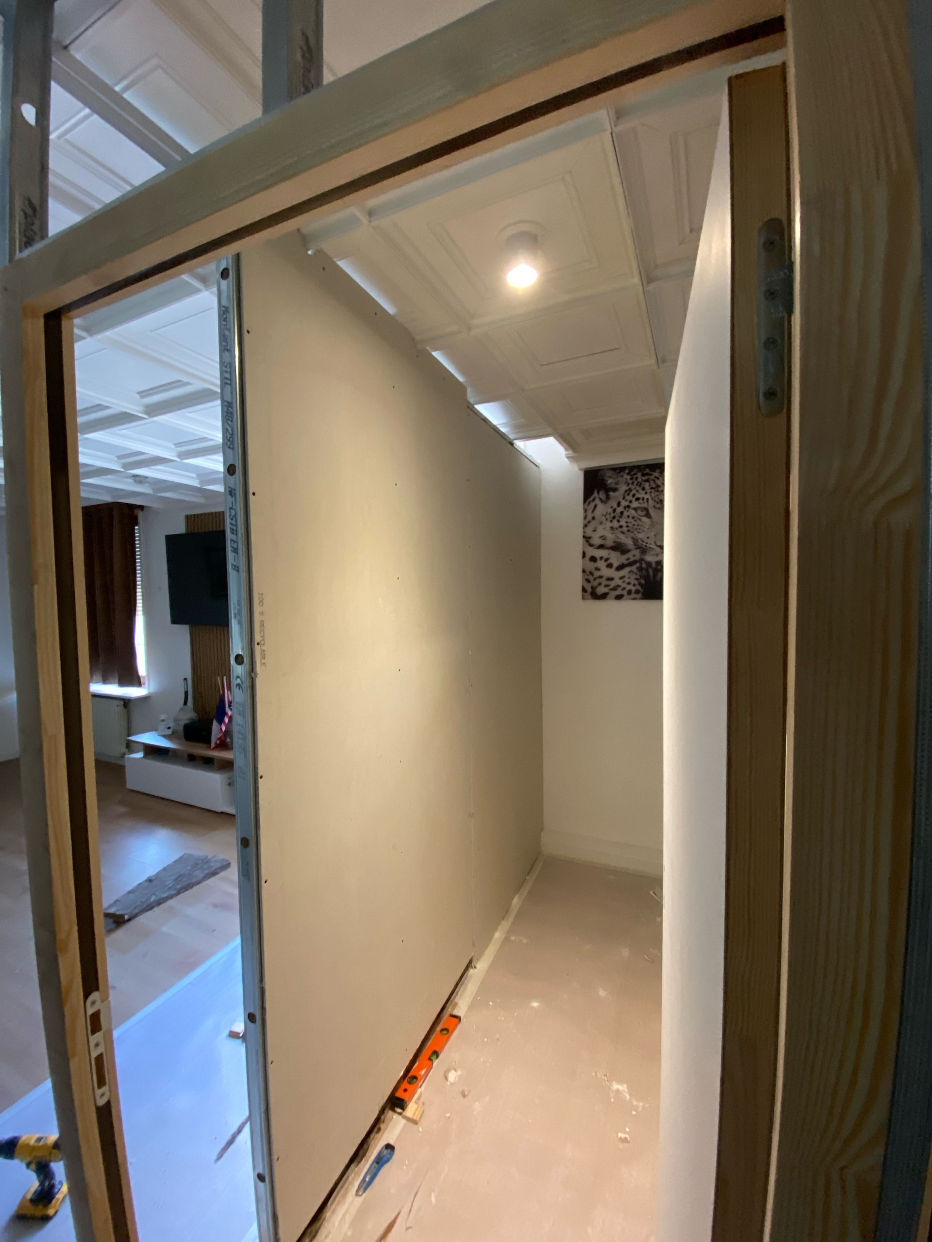 Couloir étroit en travaux, murs blancs, luminaires apparents au plafond et outils au sol.