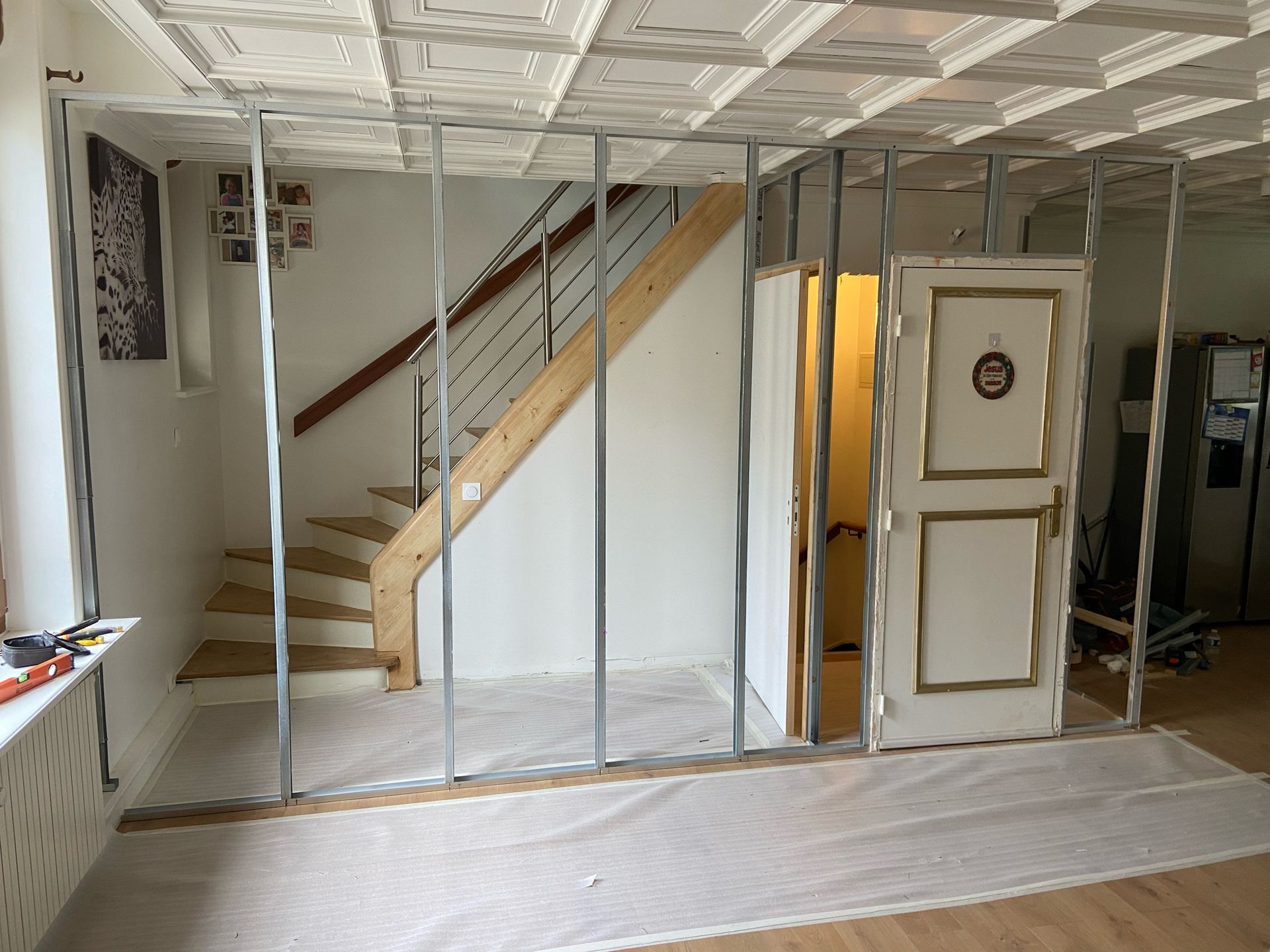 Rénovation intérieure avec montants muraux apparents, escalier et porte blanche dans une pièce partiellement aménagée.