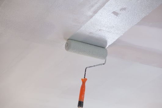Rouleau à peinture appliquant de la peinture blanche sur un bord de plafond.