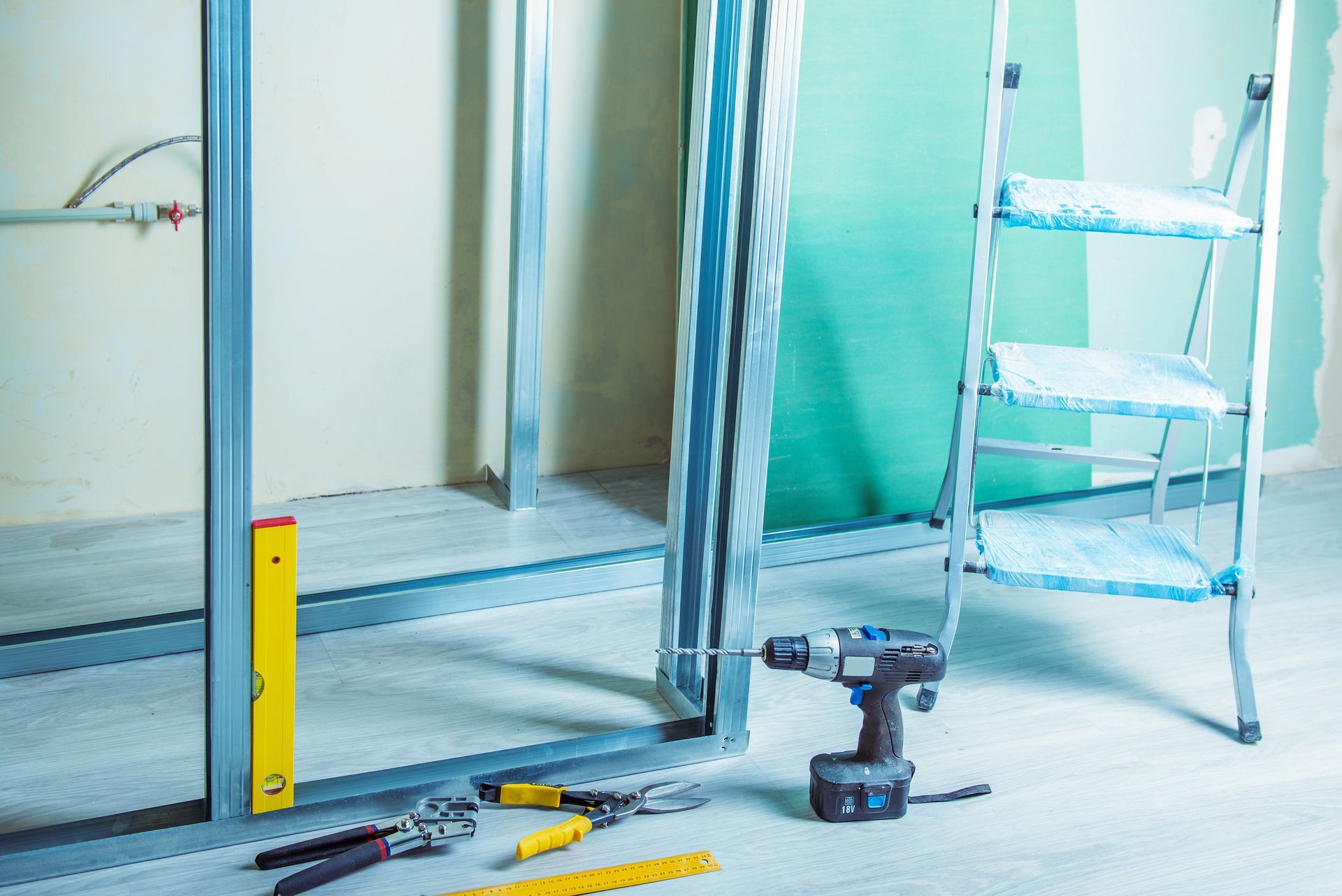 Salle de bains en construction avec outils, échelle et cadre de douche dans une pièce bleu clair.