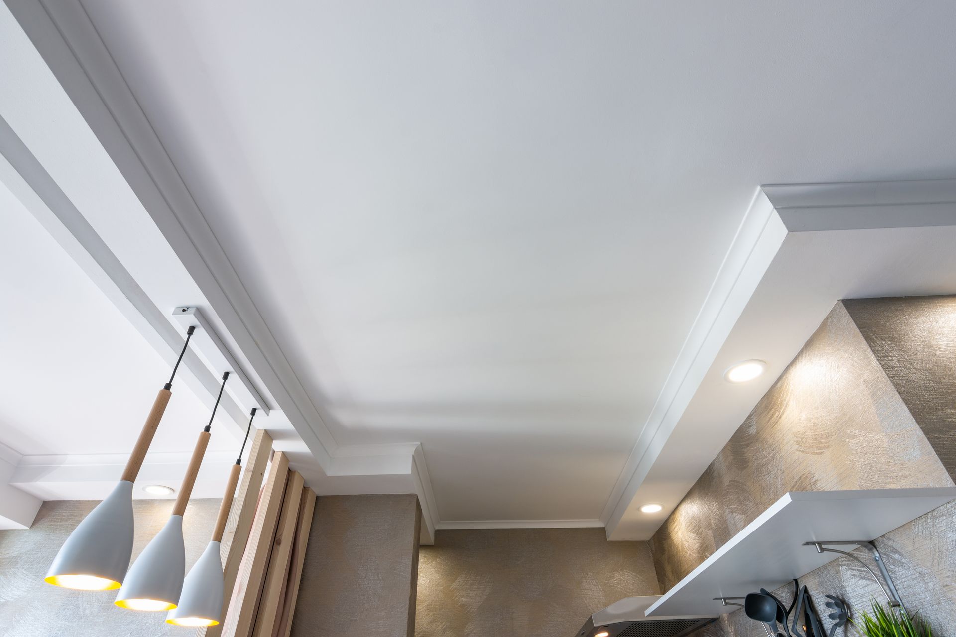Plafond de cuisine moderne avec spots encastrés, suspensions et moulures gris clair, vu d'en bas.
