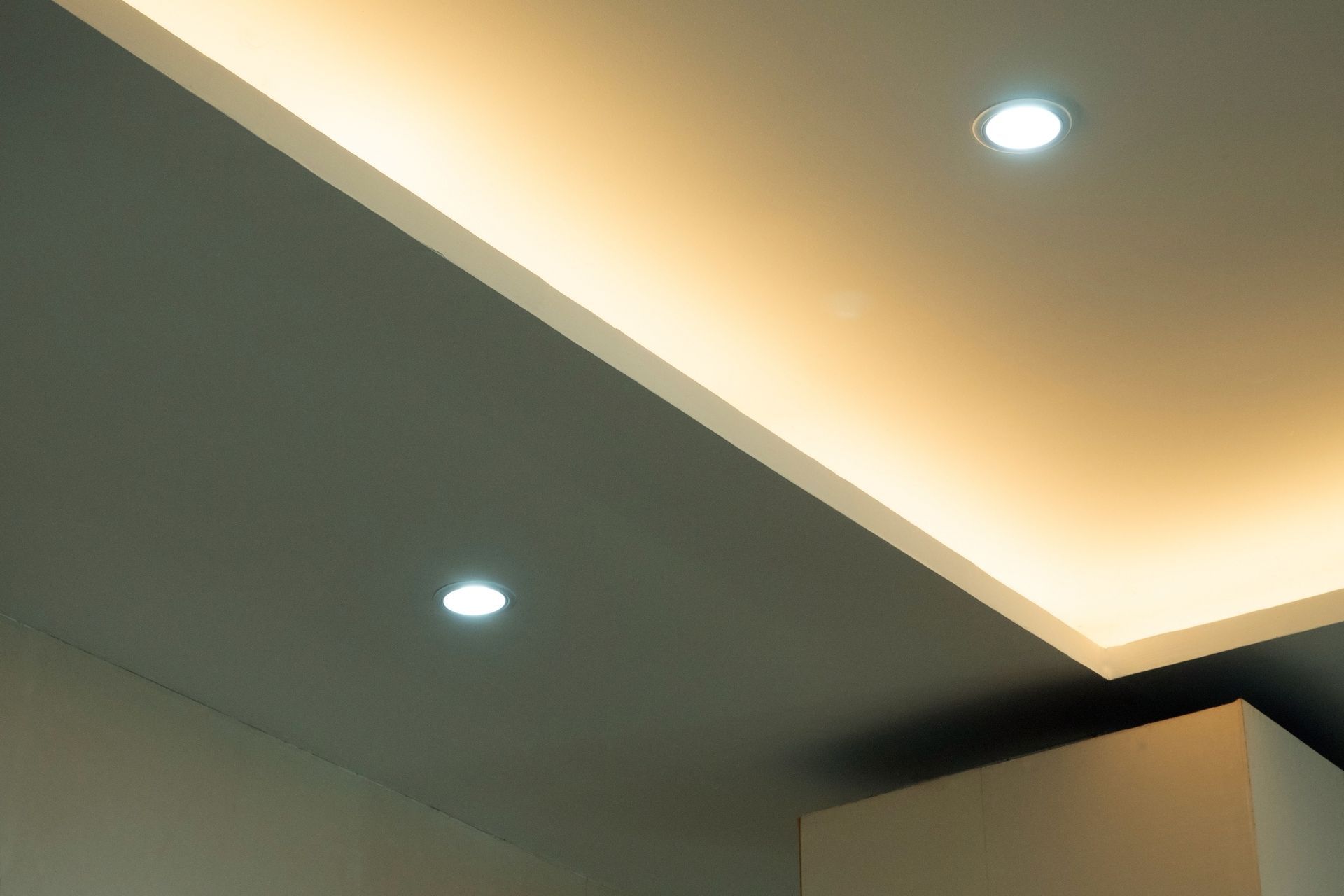 Plafond moderne avec spots encastrés et éclairage indirect chaleureux dans un coin de la pièce.