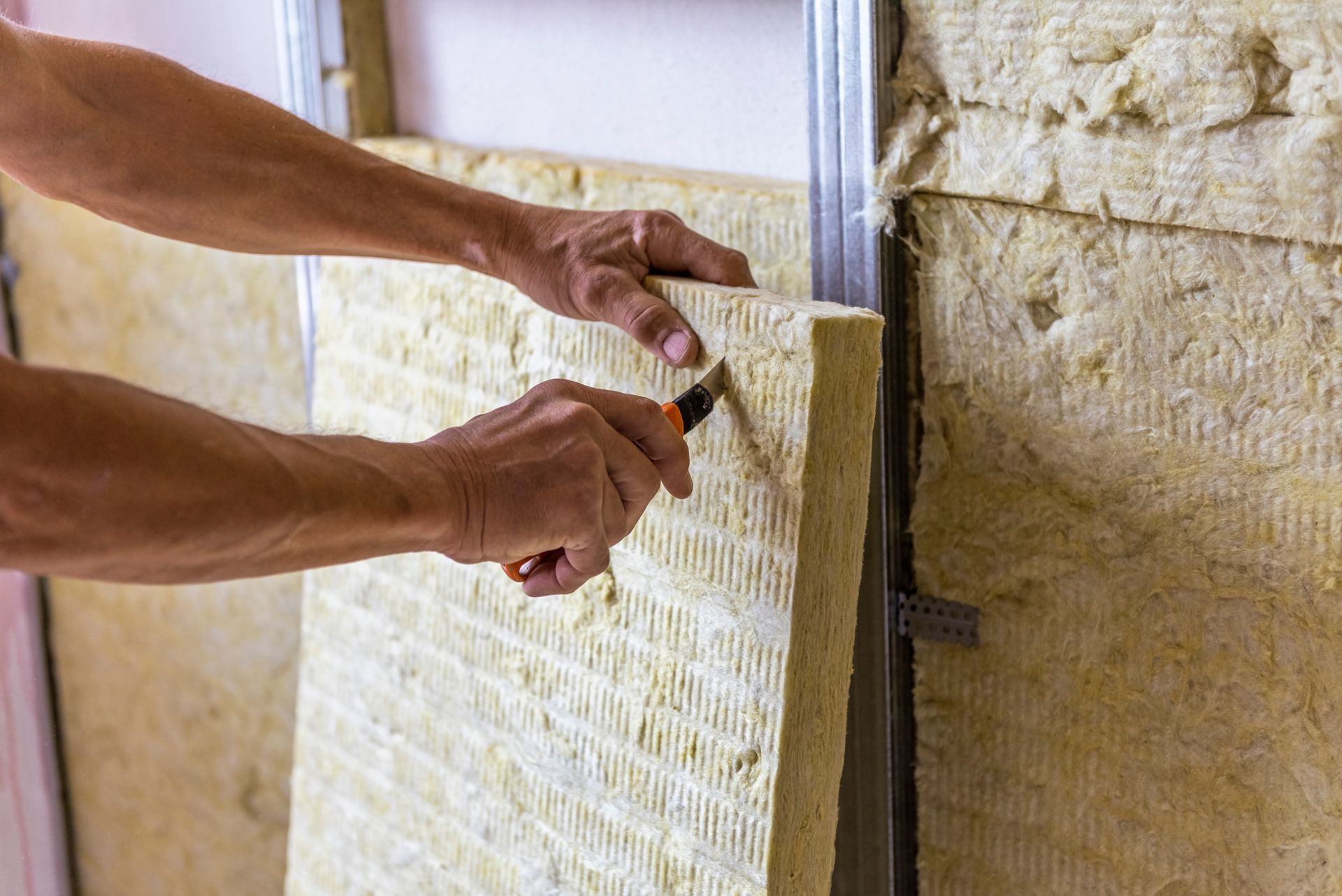 Mains installant des rouleaux d'isolant dans une cavité murale avec un cutter.