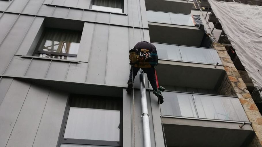 Cordiste installant un conduit de gouttière sur un immeuble 