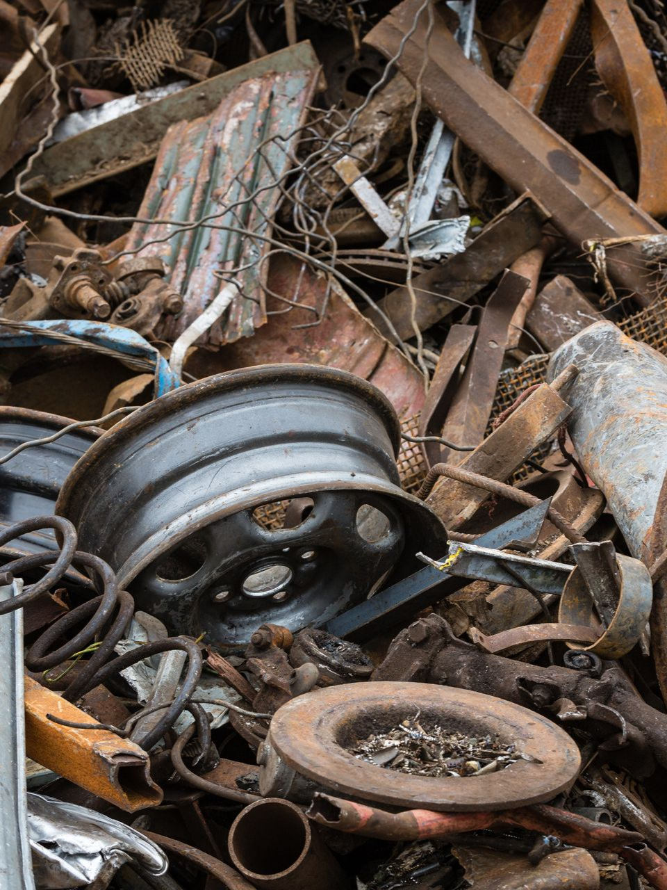 Tas de ferraille, comprenant une jante de roue de voiture et un disque de frein, à l'extérieur.