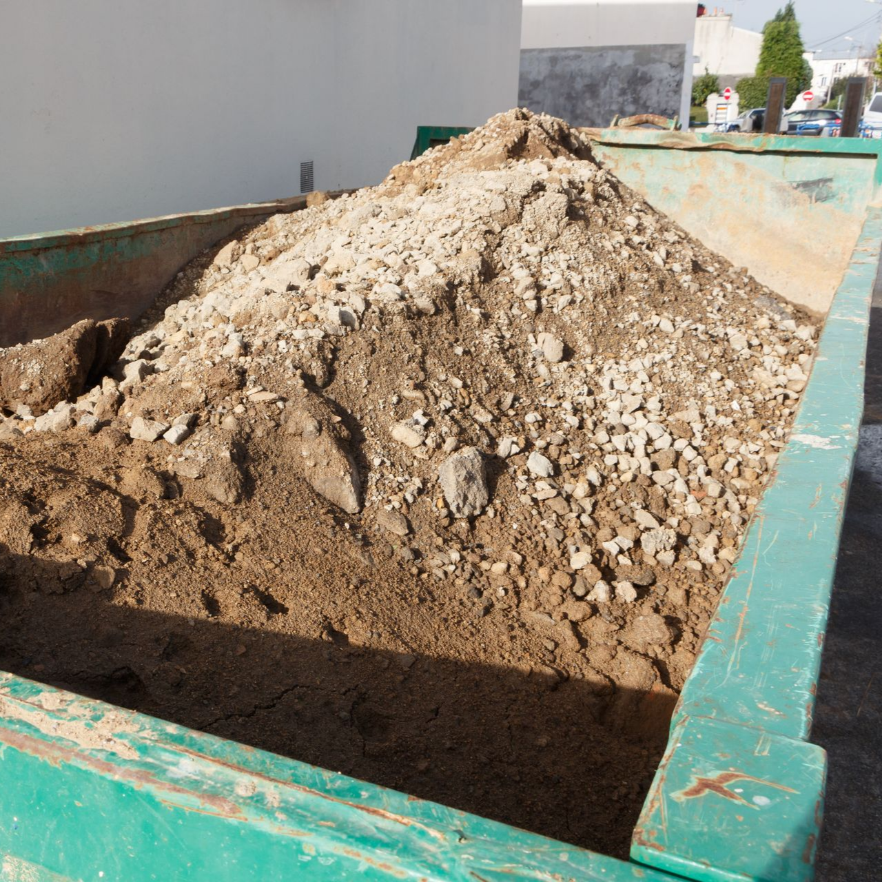 Benne à déchets de chantier remplie de terre et de pierres.