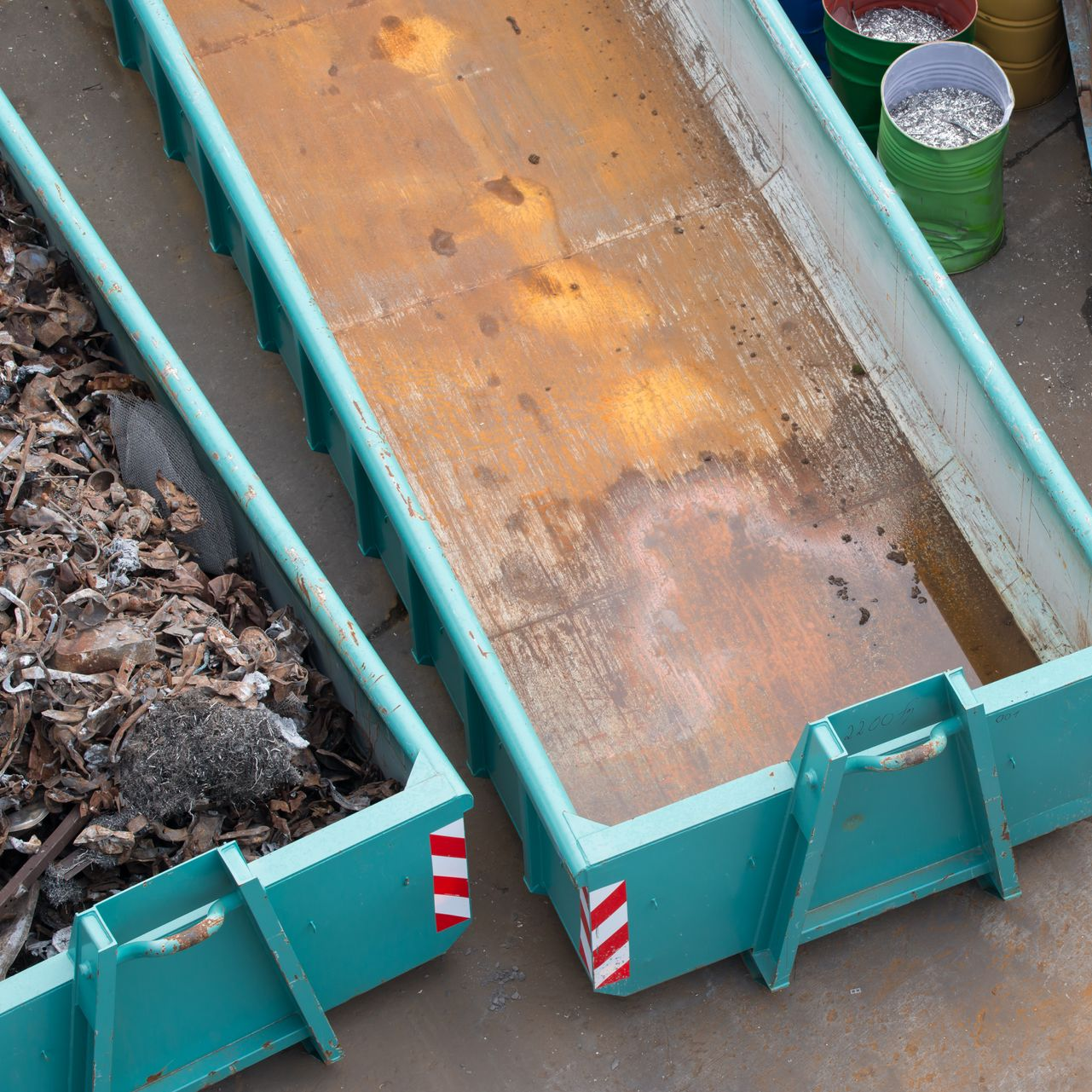 Deux bennes à ordures en métal, l'une pleine de débris, l'autre vide avec un fond rouillé.
