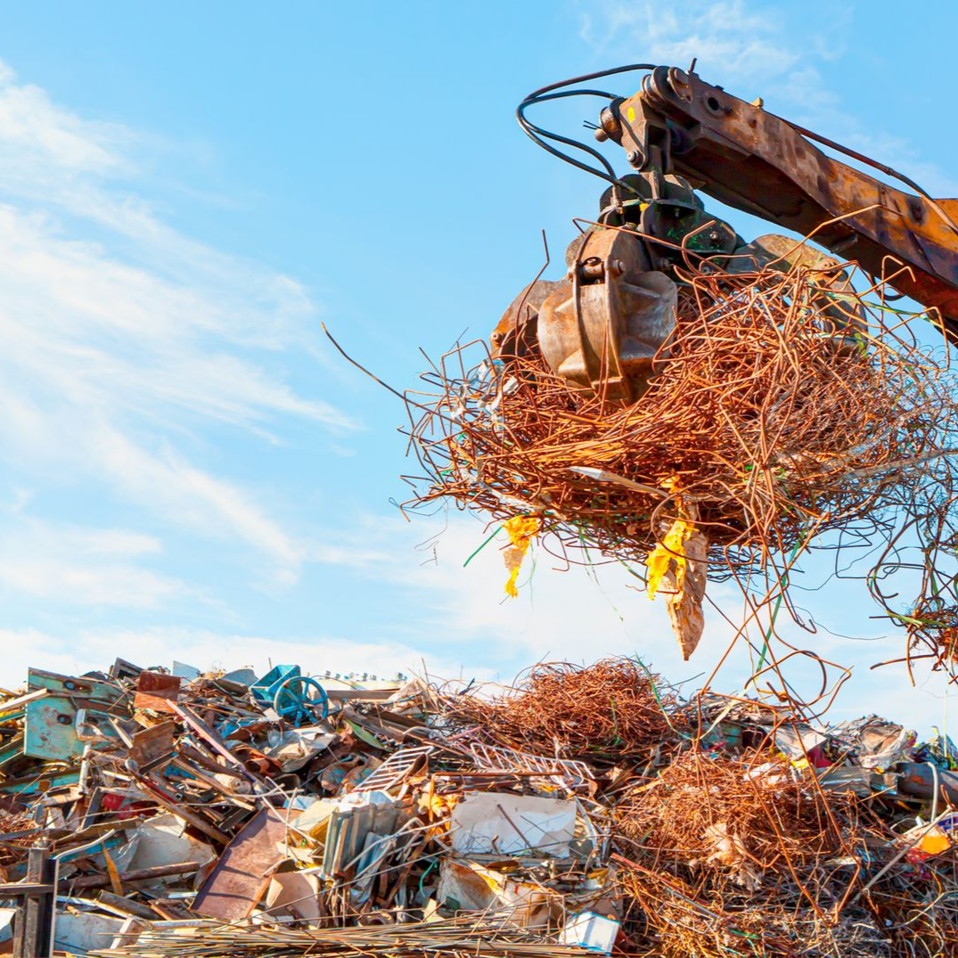 Une grue à griffes soulève un tas de ferraille.