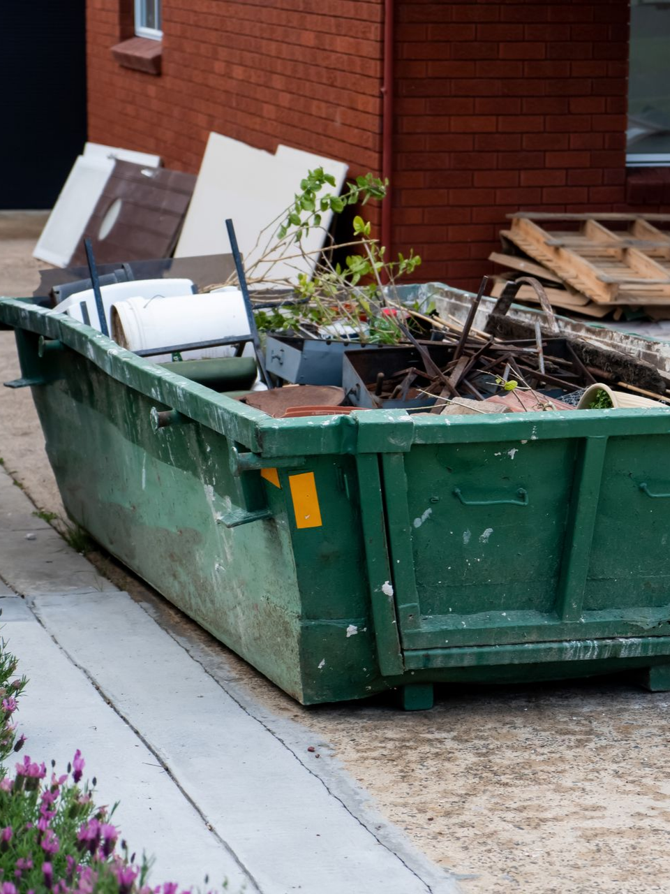 Une benne à ordures verte remplie de débris est posée sur du béton.