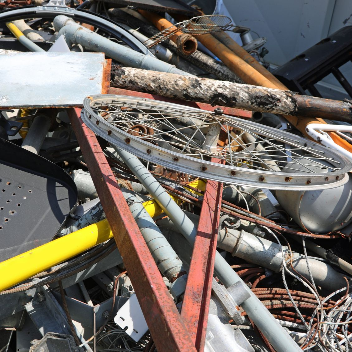 Tas de ferraille comprenant une roue de vélo, des tuyaux et des poutres.