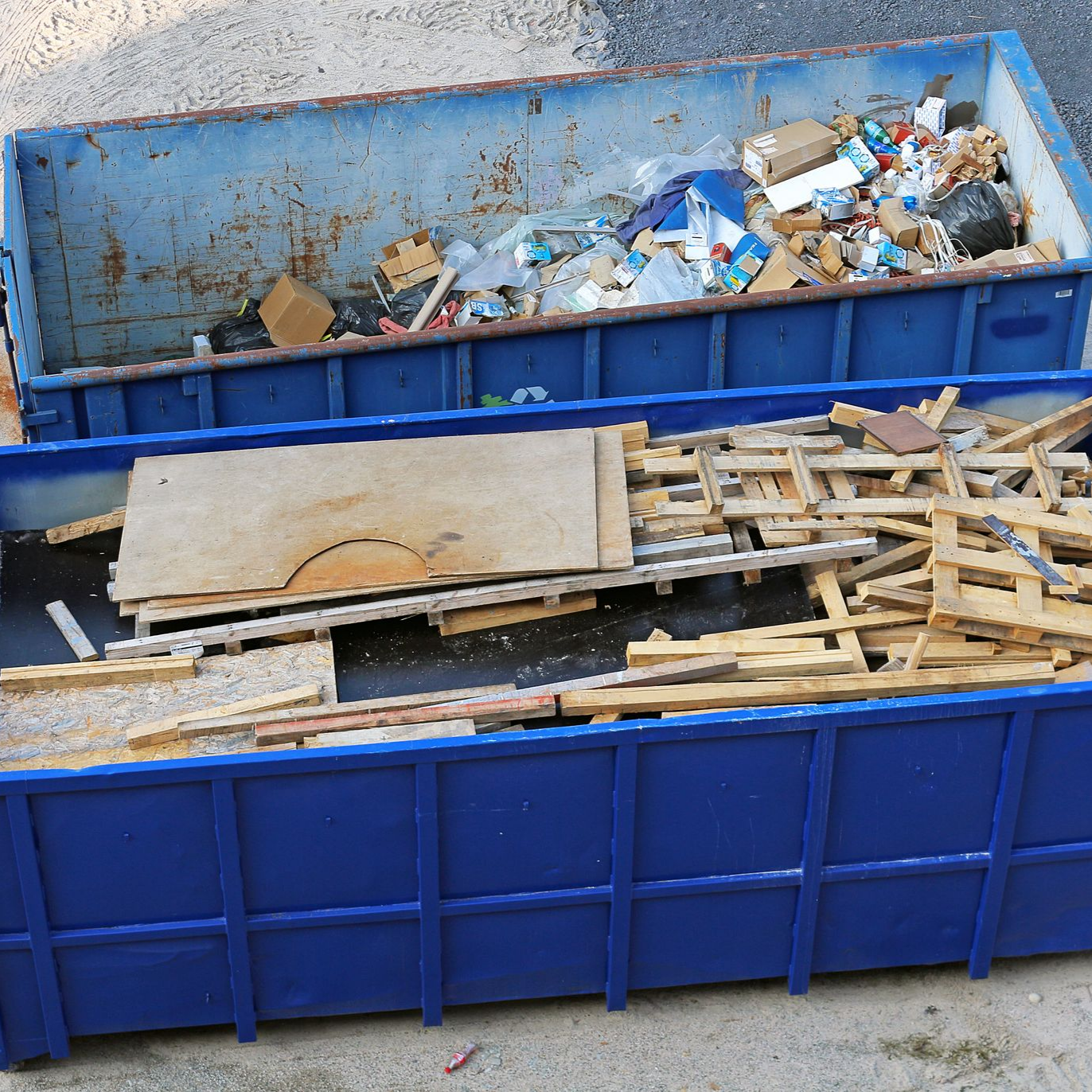 Deux bennes bleues remplies d'ordures et de débris de construction.