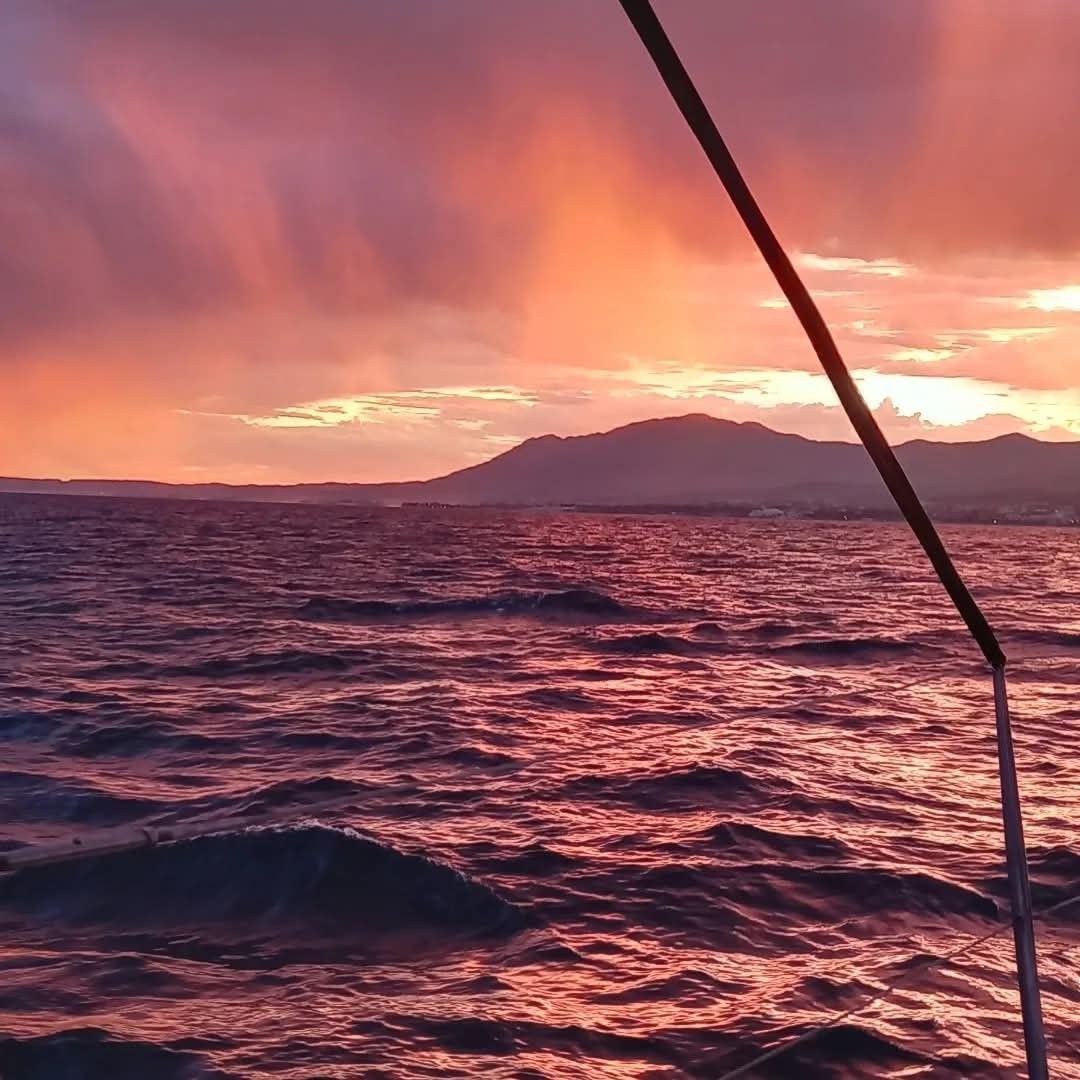 A dramatic, fiery pink and orange sunset over a choppy ocean, viewed from the side of a boat with a visible railing.