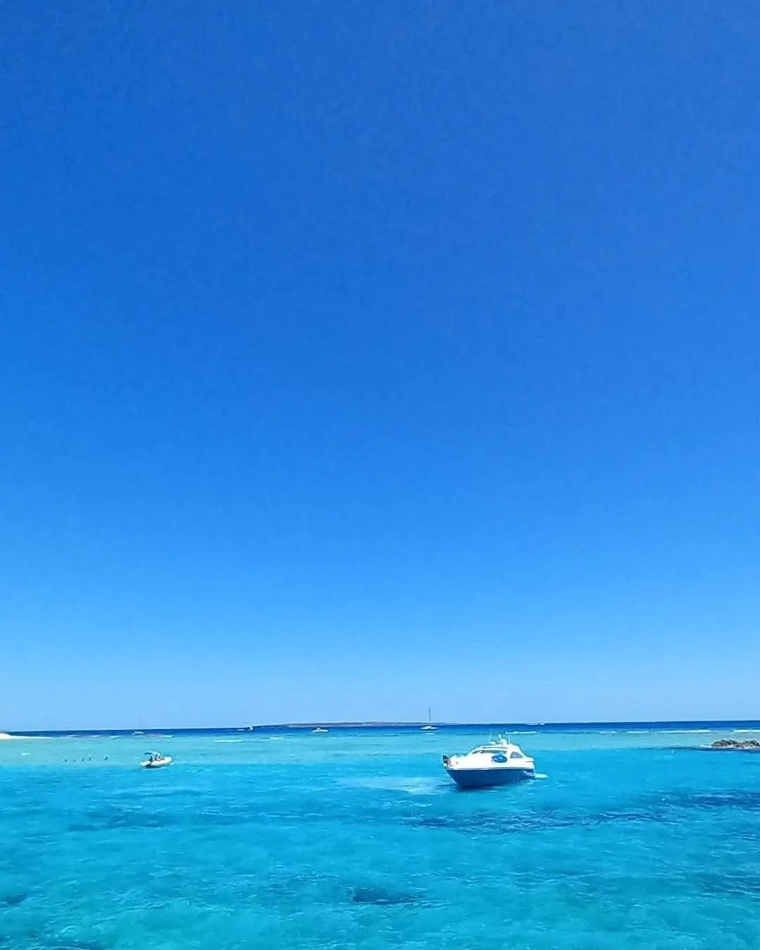 A motorboat sits on vibrant, clear turquoise water under a vast, cloudless deep blue sky.