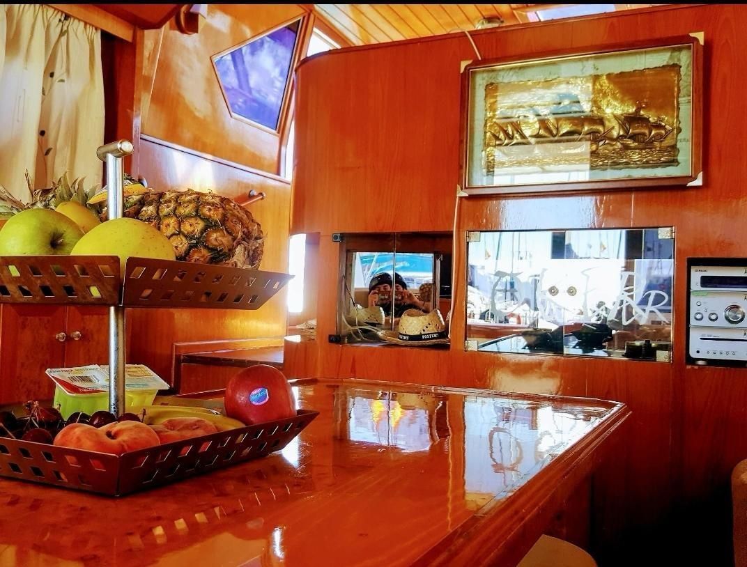 A tiered fruit stand with apples, pears, and a pineapple sits on a polished orange-wood counter in a wood-paneled room.