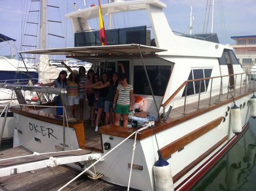 A group of people standing on the deck of a white boat docked in a marina.