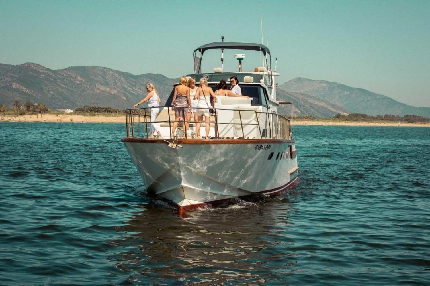 A group of people standing on the deck of a white boat cruising on the water with mountains in the background.