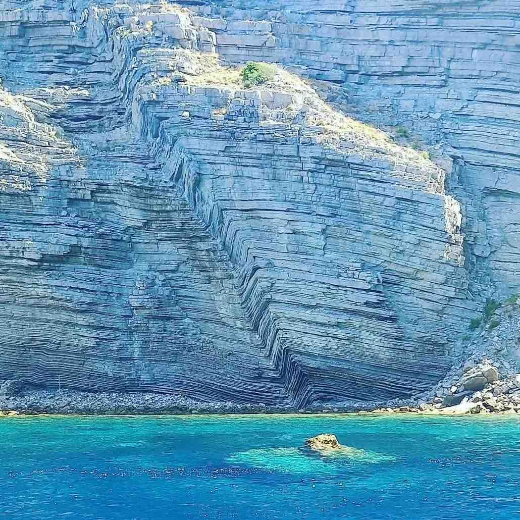 A rugged, light-colored limestone cliff face rising above clear, bright turquoise waters.