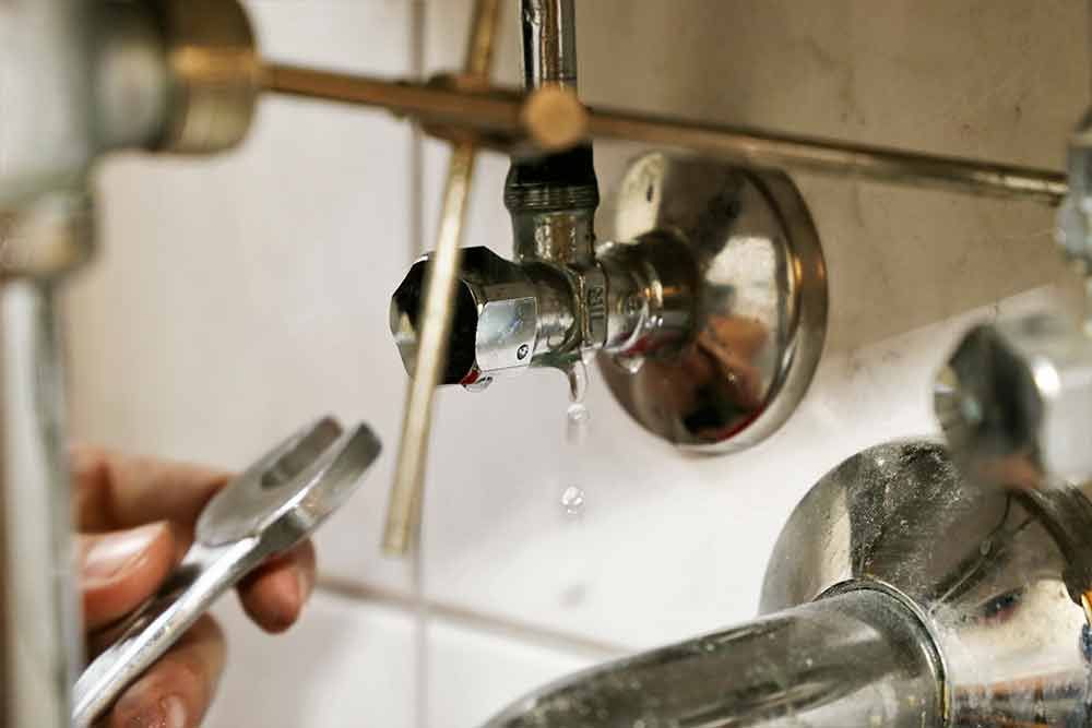 Eine Person repariert einen undichten Wasserhahn mit einem Schraubenschlüssel.