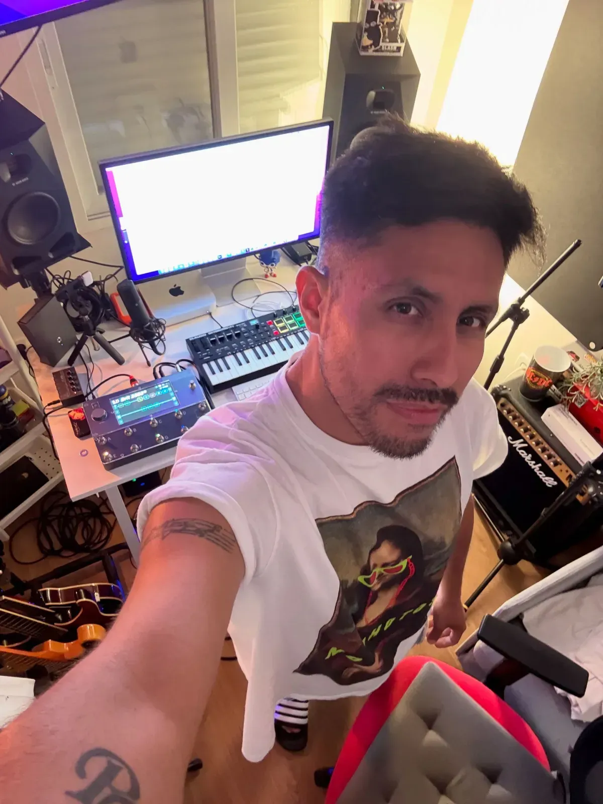 Un hombre con una camiseta estampada se toma una selfie en un estudio de música casero