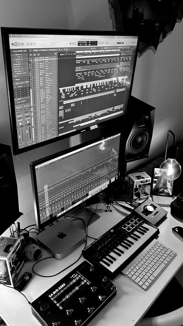 Un estudio de producción musical casero con dos monitores, un teclado MIDI y equipo de audio sobre un escritorio blanco.