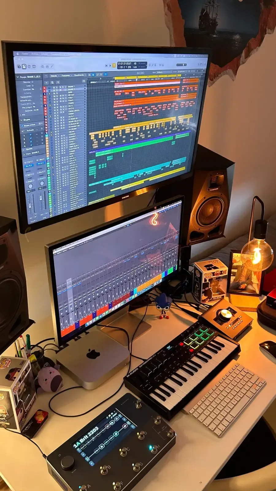 Un estudio de producción musical casero con dos monitores de ordenador apilados que muestran una estación de trabajo