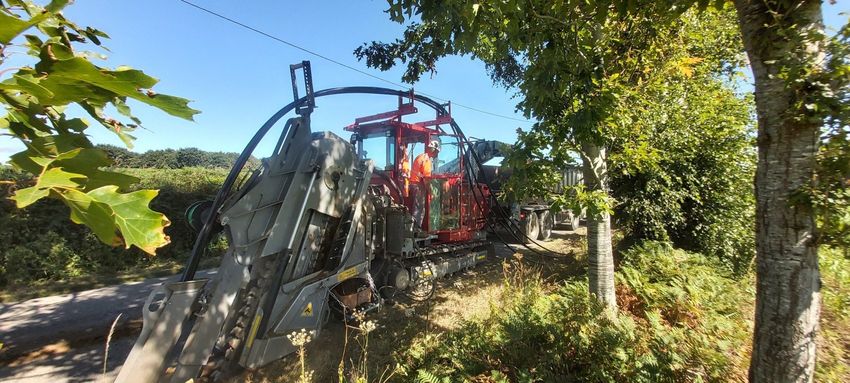 Machine de travaux publics en cours d'utilisation dans un champ au bord d'une route