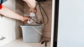 Un fontanero está arreglando un desagüe debajo de un fregadero en una cocina.