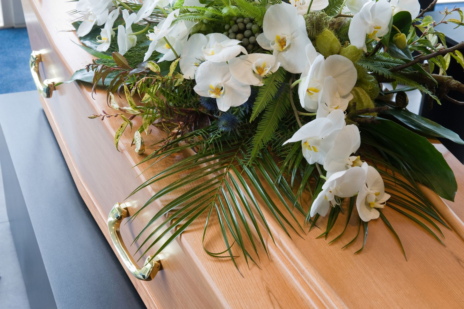 Cercueil en bois clair avec des poignées dorées et recouvert de fleurs