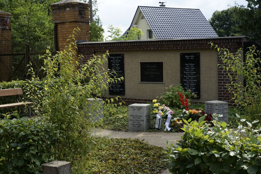 bepflanzter Bereich des Friedhofs mit Gedenktafeln an Gebäude