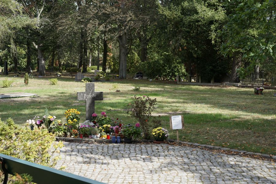 mit Blumen geschmücktes Grab mit Kreuz aus Stein