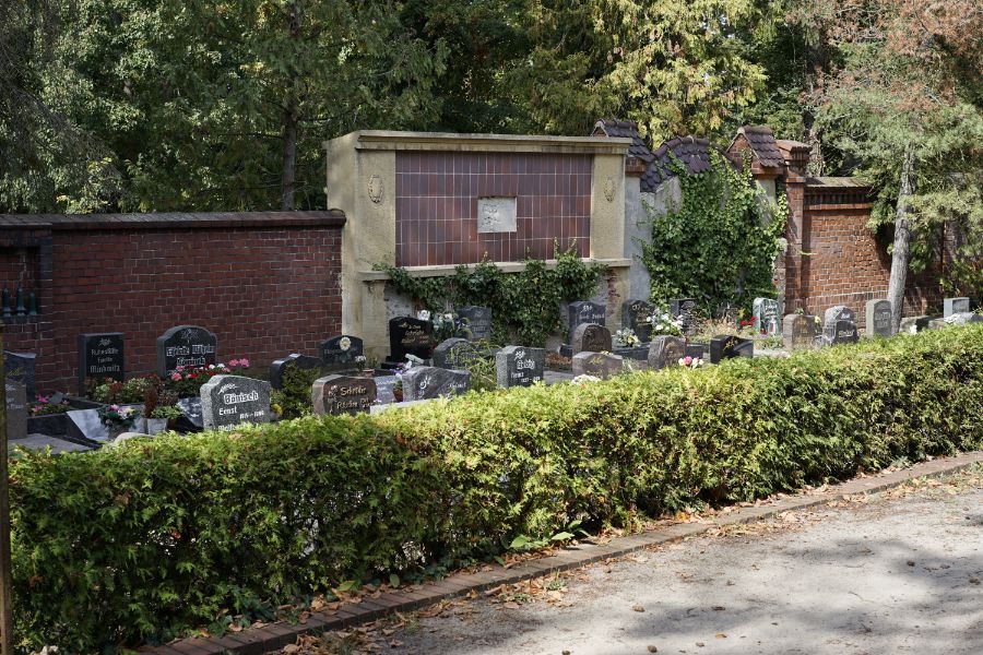 durch niedrige Hecke abgegrenzter Teil des Friedhofs mit Gräbern