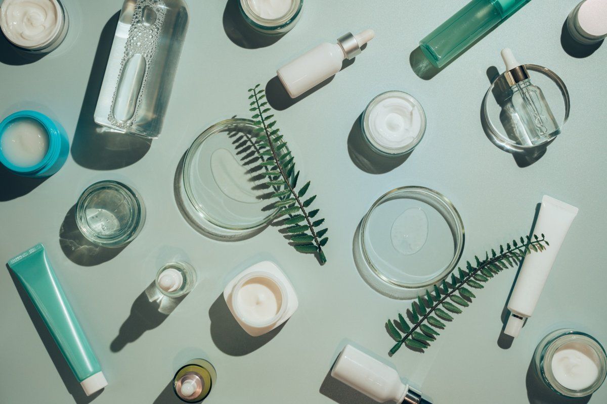 Productos para el cuidado de la piel, botellas de vidrio, frascos y tubos dispuestos sobre una superficie de color azul 