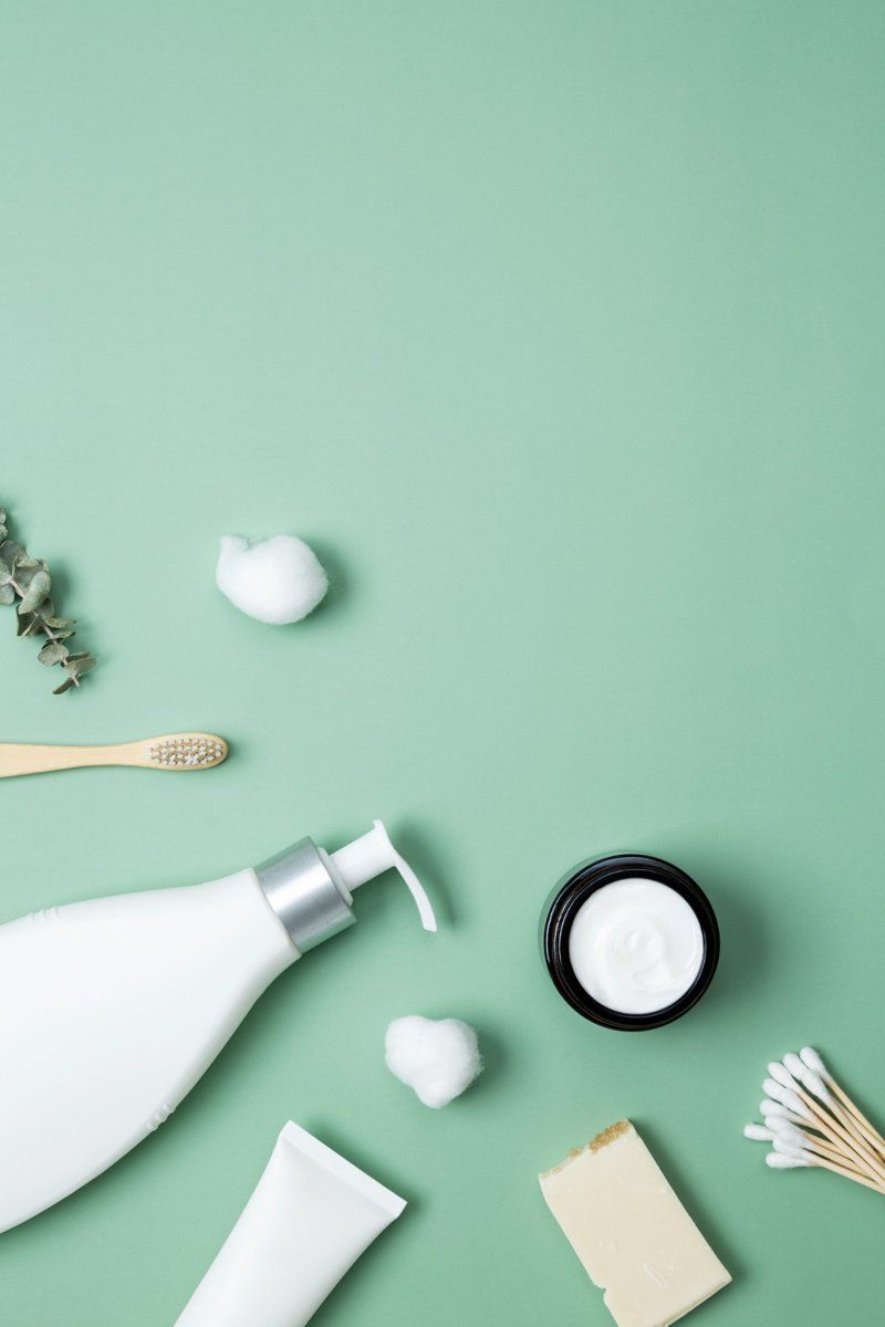 Artículos de aseo de color blanco (cepillo de dientes, jabón, crema) sobre un fondo verde claro.