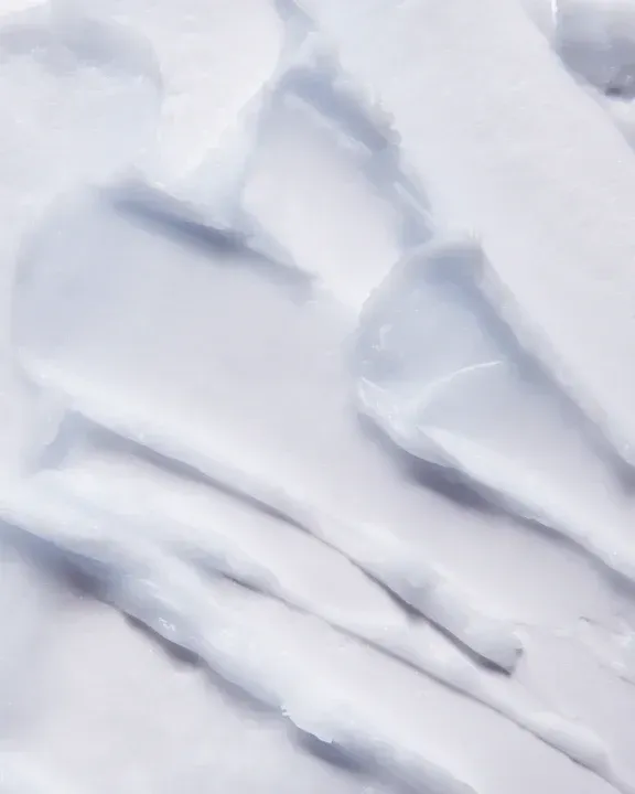 Crema blanca, posiblemente loción o humectante, extendida sobre una superficie con trazos texturizados.