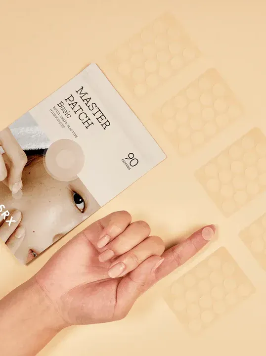 Una mano señala un parche de grano al lado de un paquete de parches para el acné.