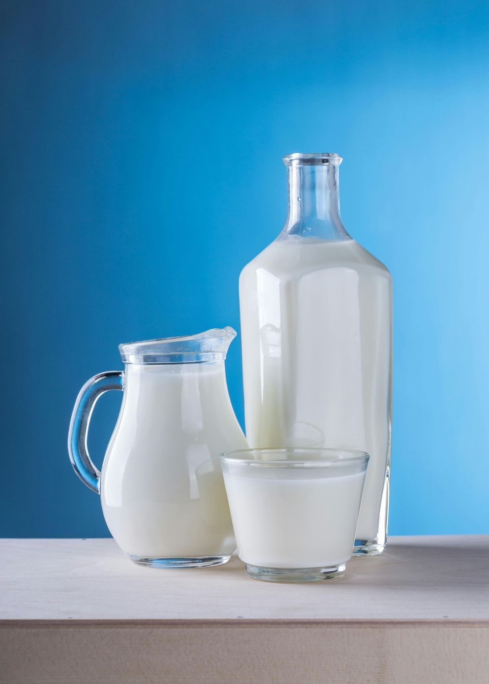 Una botella de leche, una jarra de leche y un vaso de leche sobre una mesa.