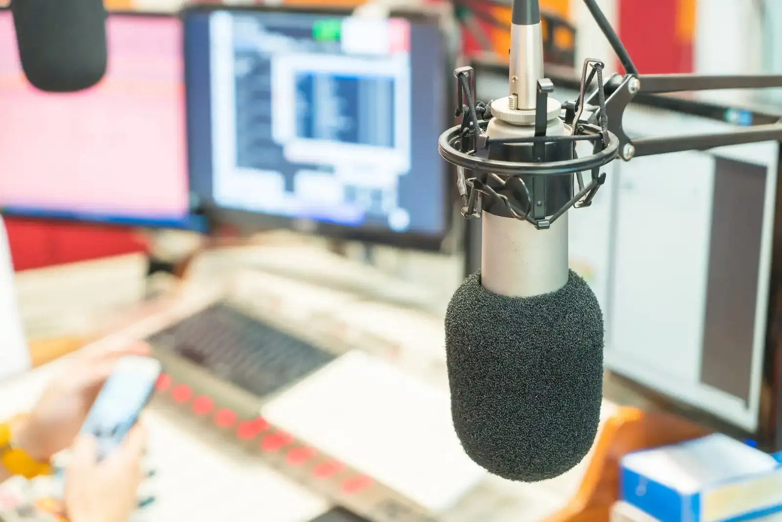 Micrófono en un estudio de radio con monitores de computadora y equipo de mezcla.
