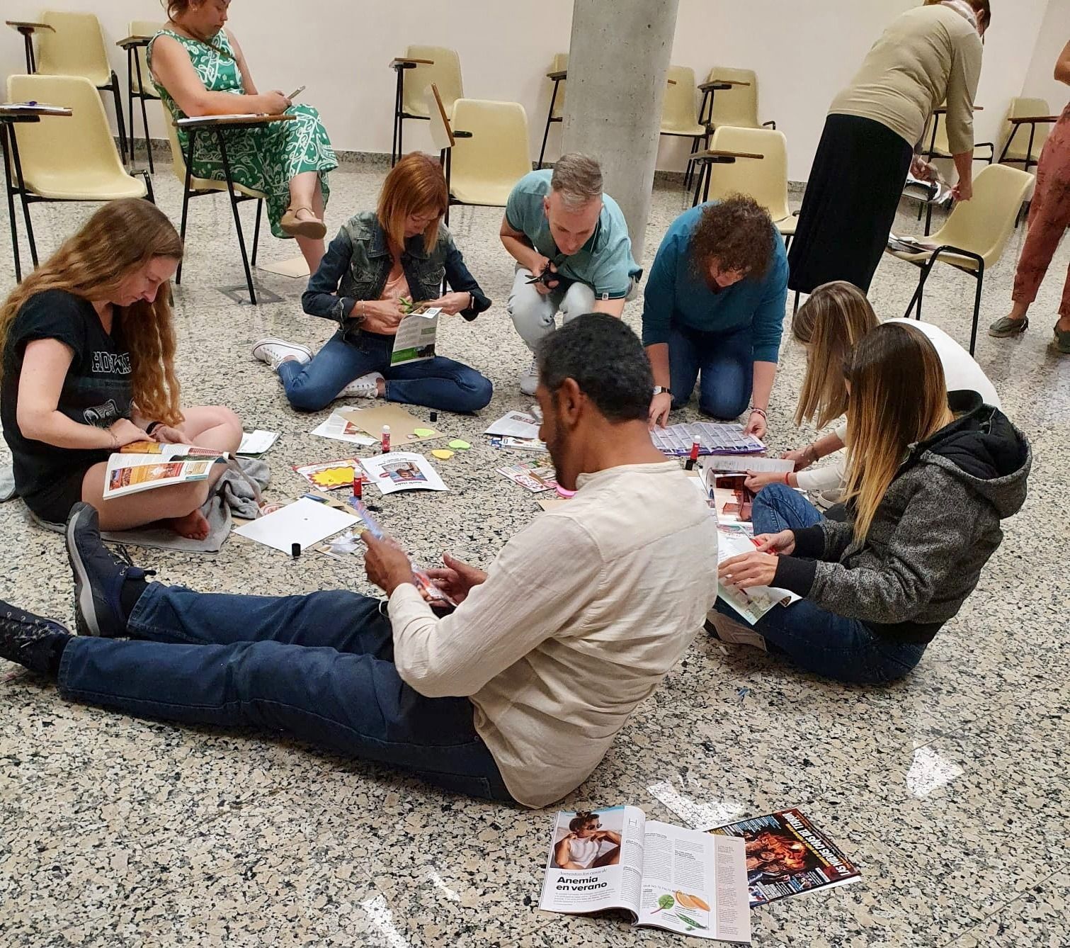 Personas sentadas y arrodilladas en el suelo, haciendo manualidades con revistas y materiales