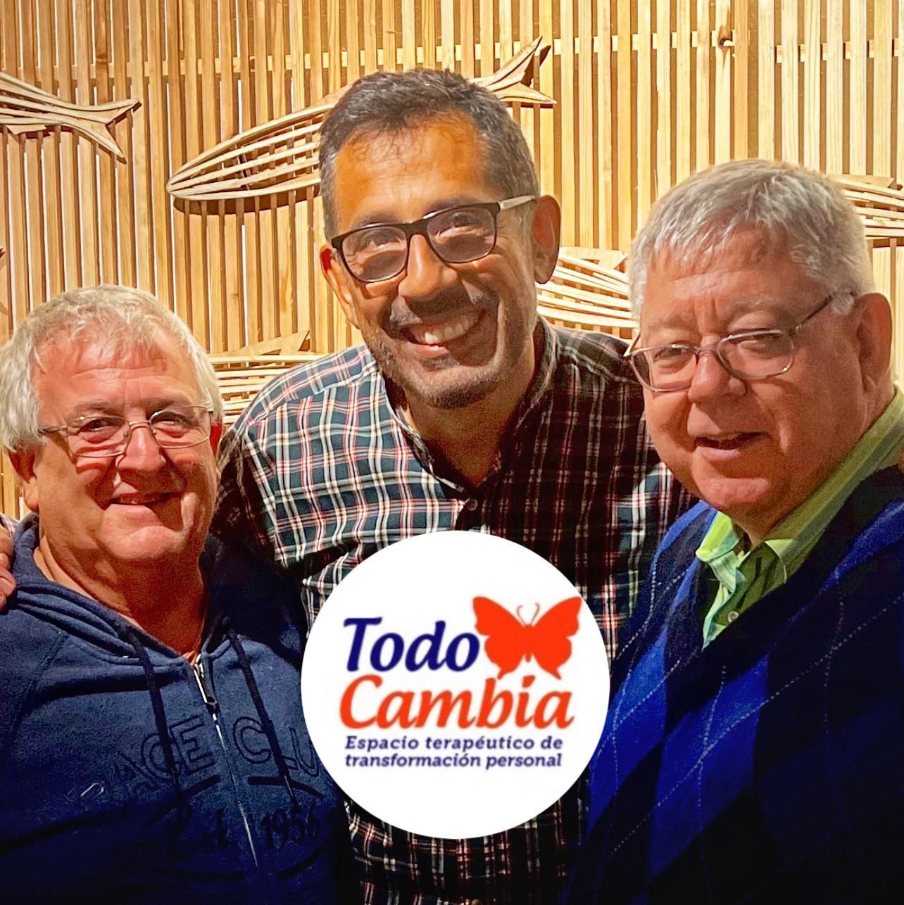 Tres hombres sonrientes, uno en el centro, frente a una pared de bambú; el logo "Todo Cambia" en primer plano.