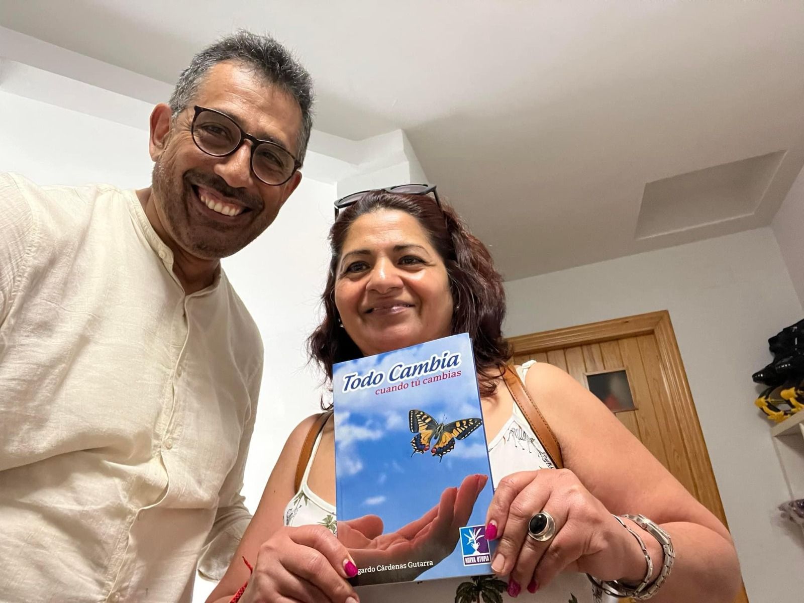 Dos personas sonriendo, sosteniendo un libro con una mariposa en la portada, en el interior.